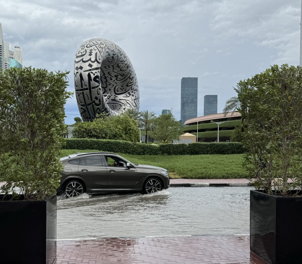 A vehicle navigates through flooded streets in Dubai, with the iconic Museum of the Future in the background, illustrating the need for Dubai Flood Recovery Technology.